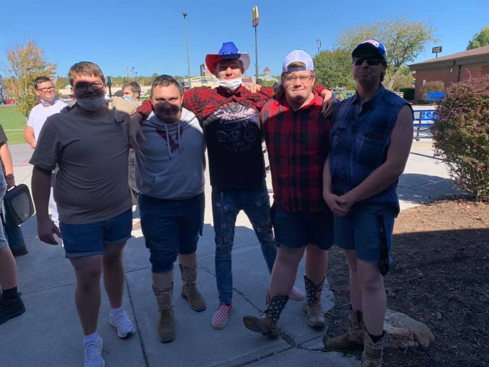 5 male students with arms around each other wearing flanel and american colored boots and hats