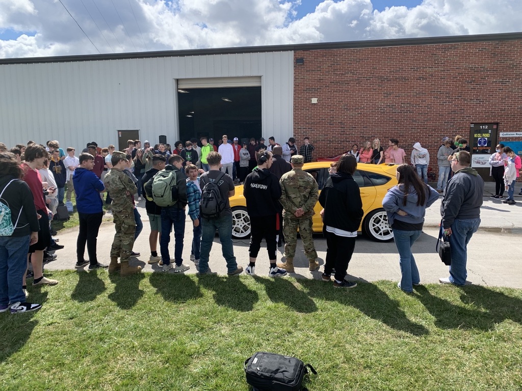students looking at yellow car outside